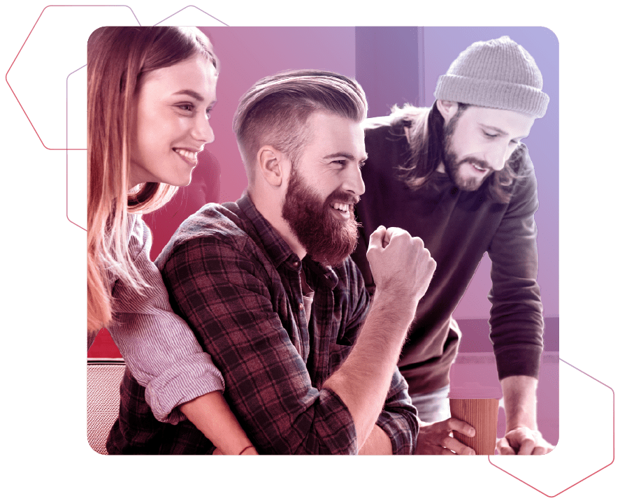 Zwei junge Männer und eine junge Frau stehen gemeinsam vor einem Tisch, während einer der Männer mit langen Haaren, Bart und Mütze auf den Tisch schaut und der andere Mann mit Bart und die Frau nach rechts lächeln auf rot-blauem Hintergrund