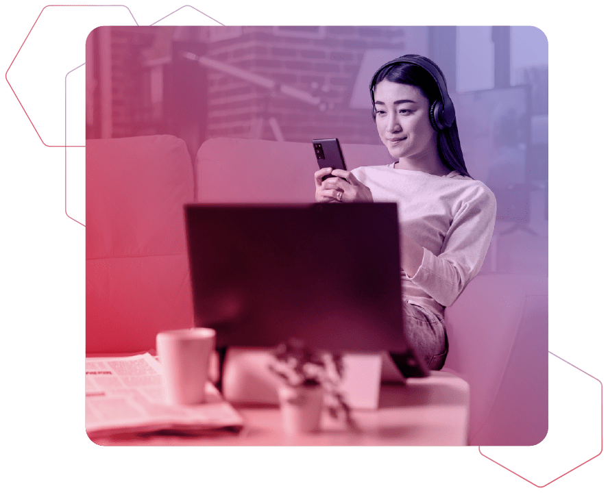 Eine Frau sitzt mit Kopfhörern auf einer Couch und schaut auf ein Smartphone auf rot-blauem Hintergrund, während der Vordergrund einen Schreibtisch und einen Monitor zeigt