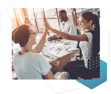 Vier junge Menschen, die an einem Tisch gemeinsam arbeiten, während sich zwei von ihnen begeistert ein High Five geben